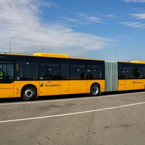 Yellow articulated city bus parked outdoors on a clear day in a spacious parking lot.