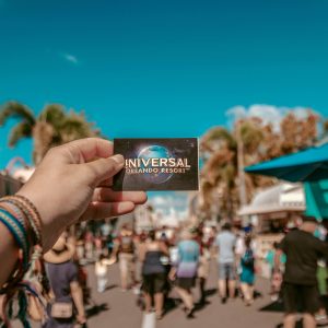 A hand holding a Universal Orlando Resort ticket in a bustling theme park setting.