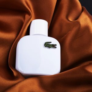 White perfume bottle with crocodile logo resting on rich brown silk, showcasing elegance and sophistication.