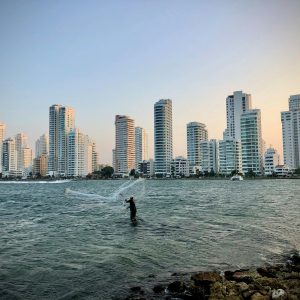 A fisherman casts his net with a city skyline in Cartagena, Colombia.